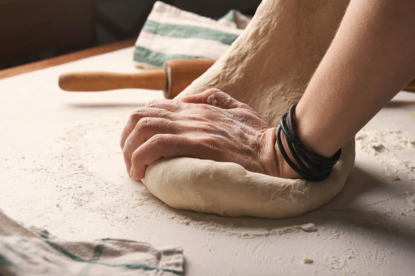 Mains qui pétrissent une pâte sur un plan de travail fariné, lumière chaude